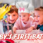 Three kids in a kitchen watch a mixer as yellow batter splashes, with a baby wearing a chef hat and pink bow; the image is overlaid with the text "BABY'S FIRST BATCH!"