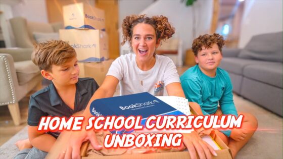 Three kids unbox a BookShark home-school curriculum box in a living room, with 'HOME SCHOOL CURRICULUM UNBOXING' text visible in the foreground.