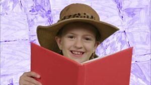 Girl wearing a wide-brimmed hat, smiling while reading a red book against a purple background.