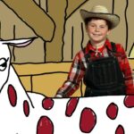 Smiling boy in a plaid shirt, overalls and a straw hat stands beside a white cow with red spots in a barn.