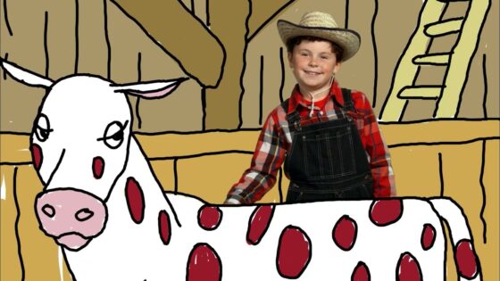 Smiling boy in a plaid shirt, overalls and a straw hat stands beside a white cow with red spots in a barn.