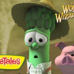 Animated VeggieTales scene: a green cucumber and a pink pig look surprised, wearing a hat, with 'The Wonderful Wizard of Ha's' logo in the corner.