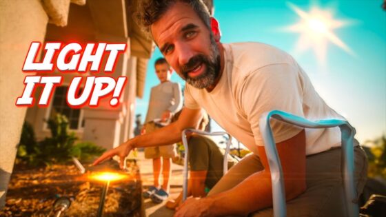 Bearded man crouching outdoors, pointing a lighter to a small flame, with bold 'LIGHT IT UP!' text on the left and a sunny sky in the background.