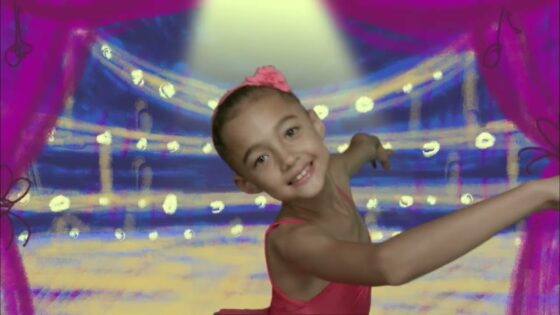 Young girl in a pink leotard posing and smiling while dancing on a bright stage backdrop with pink curtains and spotlights.