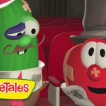Green cucumber with a mustache and top hat sits beside a red tomato with a hat in a theater row, VeggieTales logo visible in front.