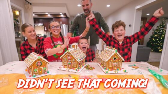 Joyful family posing with decorated gingerbread houses on a kitchen table during Christmas, a man stands behind them applauding as kids cheer.