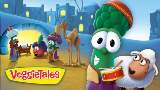 Animated VeggieTales scene with a green broccoli drummer and a sheep on a sandy town square, bright colors in the background.