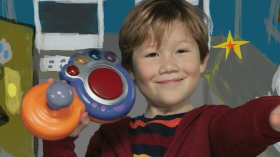 Smiling boy holds a colorful toy with an orange ring and purple buttons toward the camera.