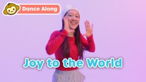 Smiling woman in a red sweatshirt waves with a purple background and the bold blue 'Joy to the World' text overlay; top-left 'Dance Along' badge present.