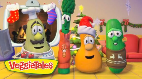 Three VeggieTales characters in holiday outfits celebrate in a festive living room with a Christmas tree and stockings.