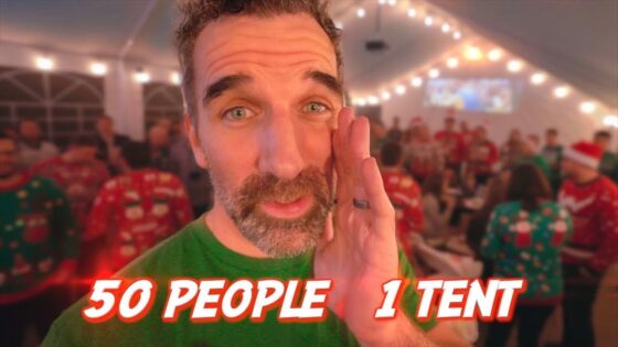 Bearded man in a green shirt in a festive tent with string lights and people in Christmas sweaters; overlay text reads '50 PEOPLE 1 TENT'