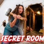 Woman with a sledgehammer breaks through a wall, revealing a wooden interior and debris on the floor; overlay reads 'A SECRET ROOM?'