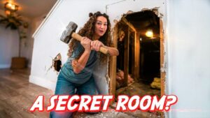 Woman with a sledgehammer breaks through a wall, revealing a wooden interior and debris on the floor; overlay reads 'A SECRET ROOM?'