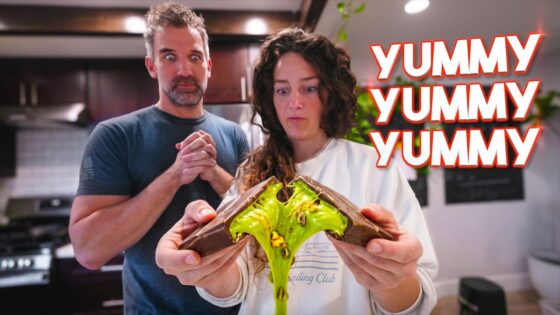 Couple in a kitchen holding a split chocolate bar with neon green goo, man looking surprised, bold YUMMY YUMMY YUMMY text on the right.