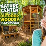 Smiling woman beside a wooden treehouse-style outdoor playground in a forest, with a mud kitchen and teepee.
