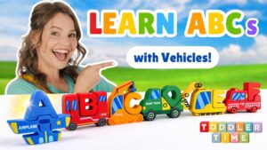 Smiling woman pointing at a row of colorful toy vehicles forming the ABCs in a bright outdoor scene, for a kids' learning video.