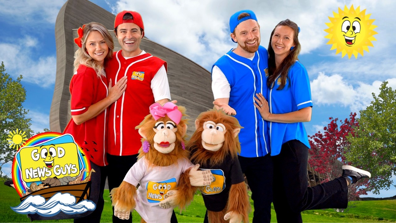 Four performers in red and blue uniforms pose with two monkey mascot characters outdoors, next to a colorful 'Good News Guys' sign and a smiling sun in the sky, conveying a family-friendly entertainment vibe.