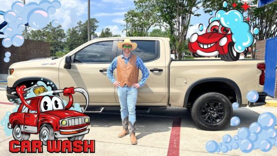 Person in a tan vest, blue shirt, jeans, and cowboy boots stands beside a beige pickup truck at a car wash, with cartoon bubbles and a red cartoon car in the foreground.
