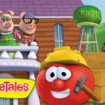 Red tomato character wearing a yellow hard hat and holding a hammer, beside stacked crates and a forklift in a construction scene.