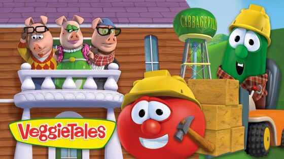 Red tomato character wearing a yellow hard hat and holding a hammer, beside stacked crates and a forklift in a construction scene.