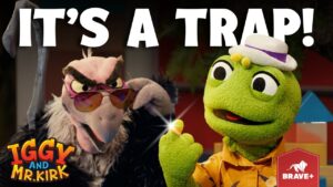 Two puppets from a kids' show in a dramatic scene: a green frog in a hat and orange shirt, and a feathery villain wearing sunglasses, with the text 'It's a trap!'